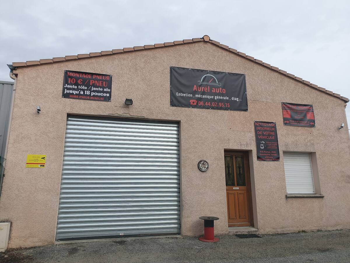La façade d'Aurél auto au 33 rue Gustave Eiffel à Crest : crépi saumon, rideau métallique, banderoles noires et porte du bureau